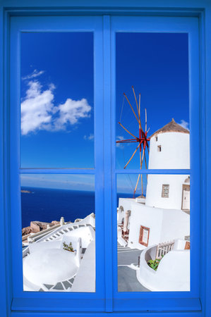 Oia village with windmill through blue window on Santorini island in Greeceの写真素材