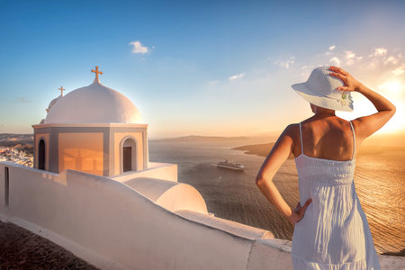 Beautiful young woman enjoying the sunset view of Thira town with church on Santorini island in Greeceの写真素材
