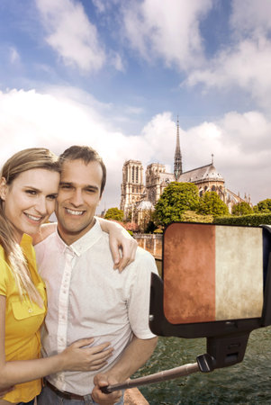 Happy couple of tourists taking selfie photo with cellphone in front of Notre Dame in Paris, Franceの写真素材