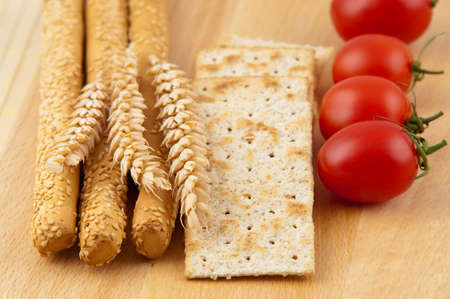 Vegetarian breakfast - tomato, crackers anf grissini arranged on a wooden plate, ready to be served 