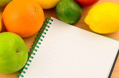 Vitamin log - various fruits, pineapple, orange, lemon and lime around notebook on a wooden deskの写真素材