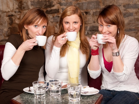 Three beautiful young students waiting drinking  coffee and having a debate in coffee shopの写真素材