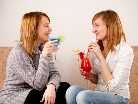 Two pretty friends celebrating with colorful cocktails on white backgroundの写真素材
