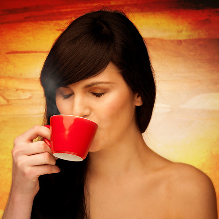 tive young woman with black hair holding red cup of coffee in her hand in the morningの写真素材