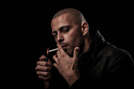 Handsome young man smokes cigarette in darkness - photography of unhealthy adicctionの写真素材