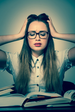 Stressed asian caucasian woman student learning in tons of books isolatedの写真素材