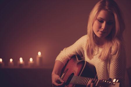 Young blonde woman playing guitar in candle light