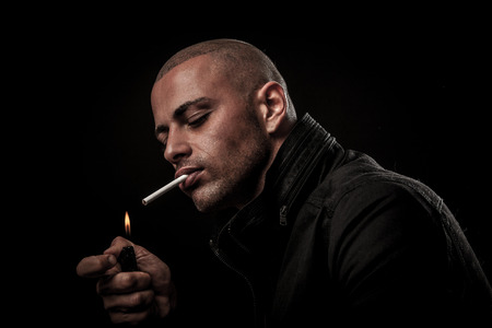 Handsome young man smokes cigarette in darkness - photography of unhealthy adicctionの写真素材