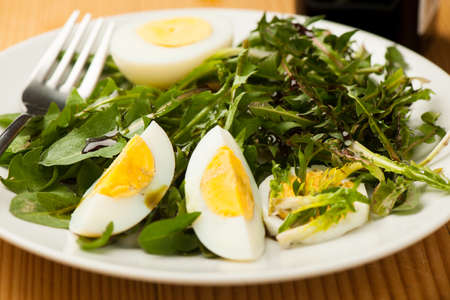 Fresh spring green dandelion salad with eggs on a plate closeupの写真素材