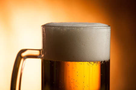 Big glass with handle filled with fresh beer with a lot of foam on top on brown backgroundの写真素材