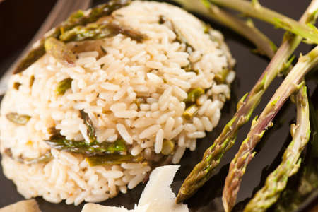Rice with wild asparagus on a blavk plate with fork served on a wooden tableの写真素材