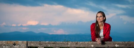 Blog style beautiful brunette woman in fashionable dress posing in park presenting garmentの写真素材