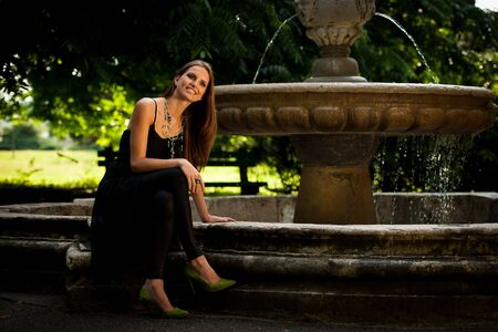 Blog style beautiful brunette woman in fashionable dress posing in park presenting garmentの写真素材