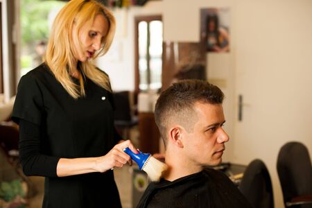 Female hairdresser cutting hair of smiling man client at beauty parlour