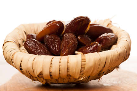 Sweet dried dates fruit in small bowl, mediterranean desert on wooden surface.