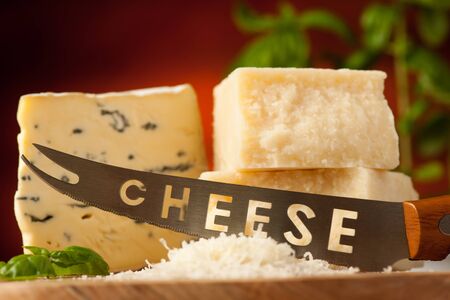 pieces of blue cheese and parmesan on a wooden cutting board being cutted with cheese knife with spices  on a wooden restaurant table in backgroundの写真素材