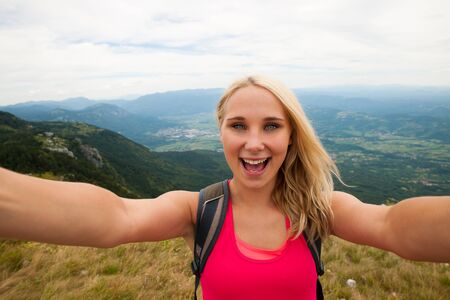 Happy woman doing selfie on top of a mountain above green valleyの写真素材