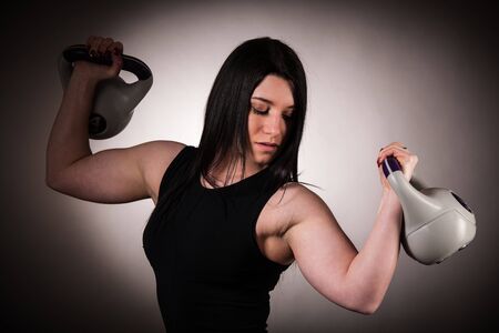 Fit woman woekout with dumbbell weight over dark studio backgroundの写真素材