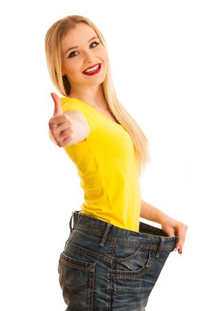 Woman gesturing success as she lost weight wearing too big trousers isolated over whiteの写真素材