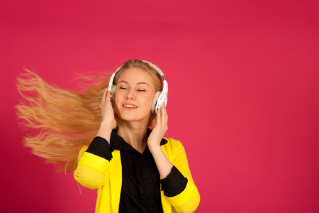 Beautiful young woman in black and yellow vibrant dress dances as she listens to the music over pink backgroundの写真素材