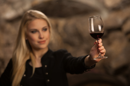Beautiful young blond woman drinks wine in wine cellarの写真素材