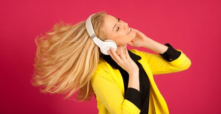 Beautiful young woman in black and yellow vibrant dress dances as she listens to the music over pink backgroundの写真素材