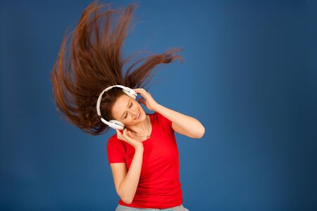 Beautiful young woman listen to the music and dance over vibrant color backgroundの写真素材