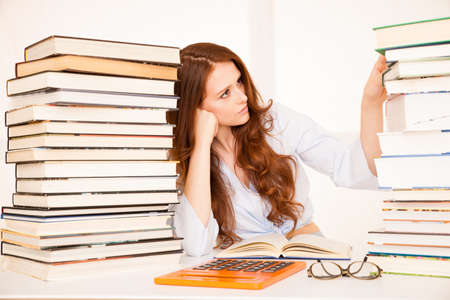 attractive young woman studies wtih hugr book piles on her desk