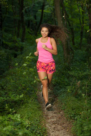 active young fit woman runs in green forest on late summer afternoon