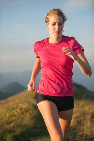 Woman runs on a top of the mountains with mountain range in backgroundの写真素材