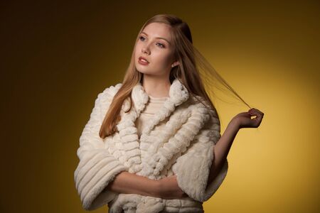 Beauty portrait of woman in fur winter jacket over yellow backgroundの写真素材