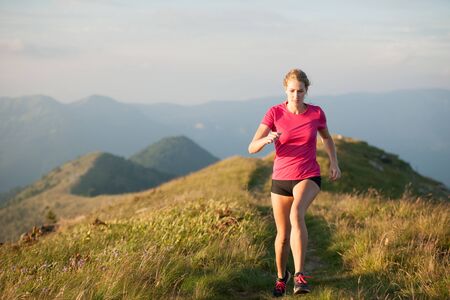 Woman runs on a top of the mountains with mountain range in backgroundの写真素材
