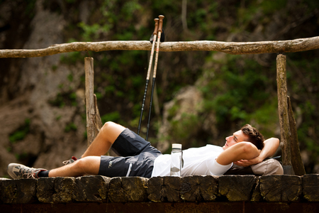 active man resting on a bridge over mountain creekの写真素材