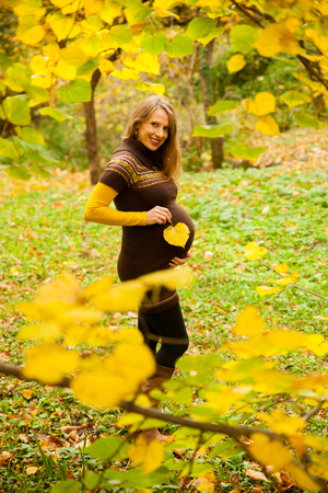 Beautiful pregnant woman outdoor in park on autumn afternoon with vibrant nature colors in background .の写真素材
