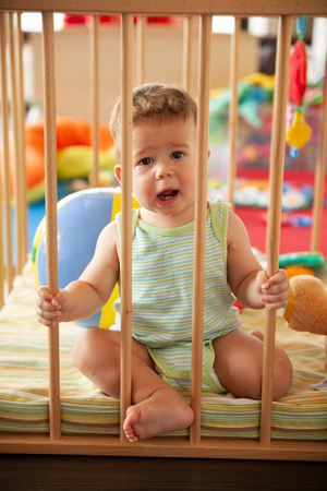 Cute smiling baby looking through the wooden bars of his crib or playpen with a happy smile indoors in the nurseryの写真素材