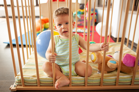 Cute smiling baby looking through the wooden bars of his crib or playpen with a happy smile indoors in the nurseryの写真素材