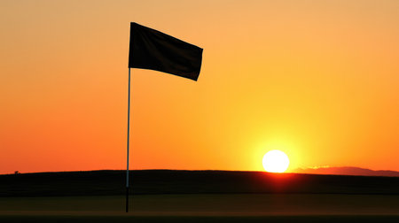 Sunset view of a golf hole, flag silhouetted against golden sky and orange-lit grassの素材