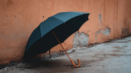 A lonely black umbrella leans against a textured orange wall, capturing the essence of urban solitude and rainy day reflections in a moody setting.の素材