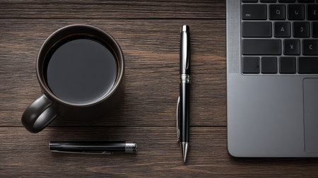 A black coffee cup, sleek laptop, and elegant pens are arranged neatly on a rustic wooden table, creating a warm and inspiring workspace ideal for enhancing productivity.の素材