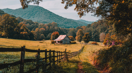 This stunning autumn landscape captures a rustic barn nestled among rolling hills and vibrant foliage. A serene pathway lined by a wooden fence invites exploration, embodying the beauty of nature in a peaceful rural setting.の素材