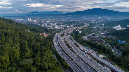 A breathtaking aerial view capturing a winding highway through lush green forests and majestic mountains at dusk, showcasing natural beauty and urban coexistence.の素材