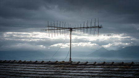 An old television antenna stands prominently atop a roof, set against a moody sky and distant mountains, capturing a nostalgic moment in rural design.の素材