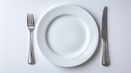 A visually appealing setup showcasing an empty white plate, fork, and knife. Perfect for illustrating gourmet dining, hospitality themes, or culinary arts.の素材