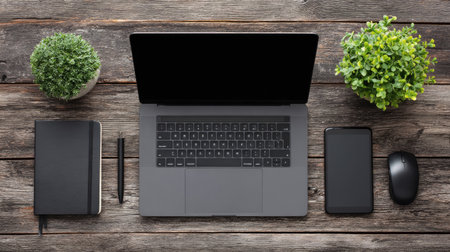 A sleek modern workspace featuring a laptop, smartphone, notebook, pen, and potted plants arranged on a rustic wooden desk, ideal for professionals.の素材