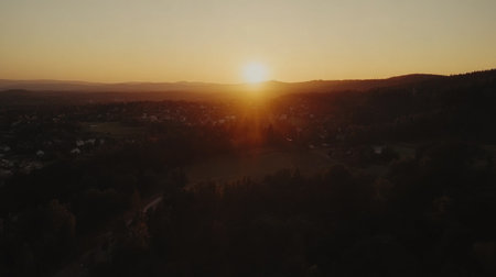 A breathtaking aerial view of a serene sunset over a quiet rural landscape. Warm golden hues fill the sky as the sun sets behind distant hills.の素材