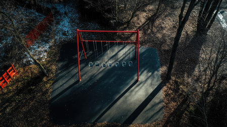 An aerial view of a vacant swing set in a serene park, surrounded by trees and shadows, evoking a sense of quiet and tranquility in nature.の素材