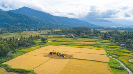 A breathtaking aerial view showcasing rice field harvesting with machinery, surrounded by lush greenery and mountains. This image captures the essence of agriculture in a serene rural setting.の素材