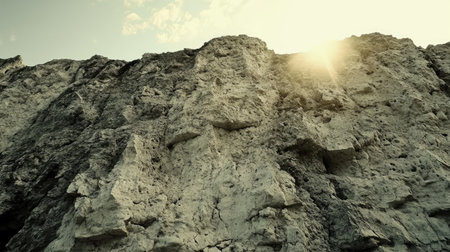 A majestic view of a rugged cliff face bathed in warm sunlight, set against a clear sky. Ideal for landscapes and nature-themed projects.の素材