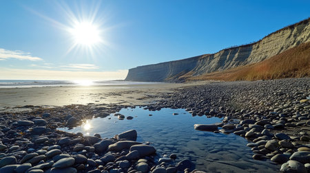 A stunning coastal scene featuring a rocky shoreline illuminated by sunlight, with a clear blue sky and tranquil waters reflecting the serene landscape.の素材