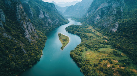 Captivating aerial shot of a winding river surrounded by lush green valleys and majestic mountains, showcasing the beauty of unspoiled nature.の素材
